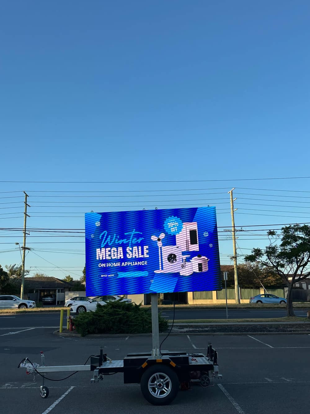 LED trailer sign in a car park showing a blue 'Winter Mega Sale' home-appliance advertisement