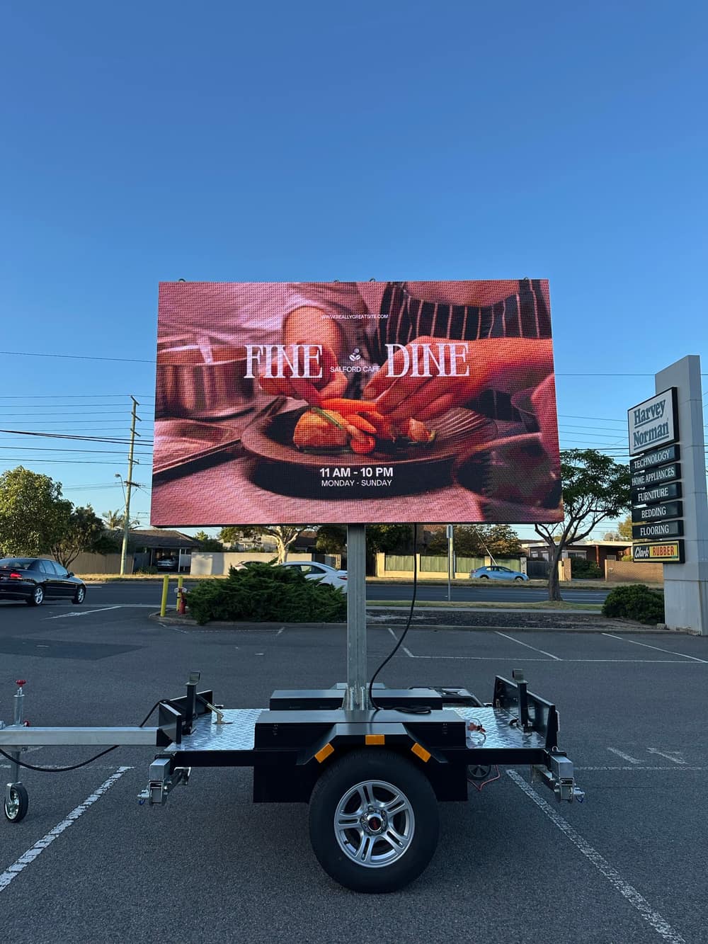 Side view of the LED trailer sign in a car park showing a full-colour restaurant advertisement with opening hours