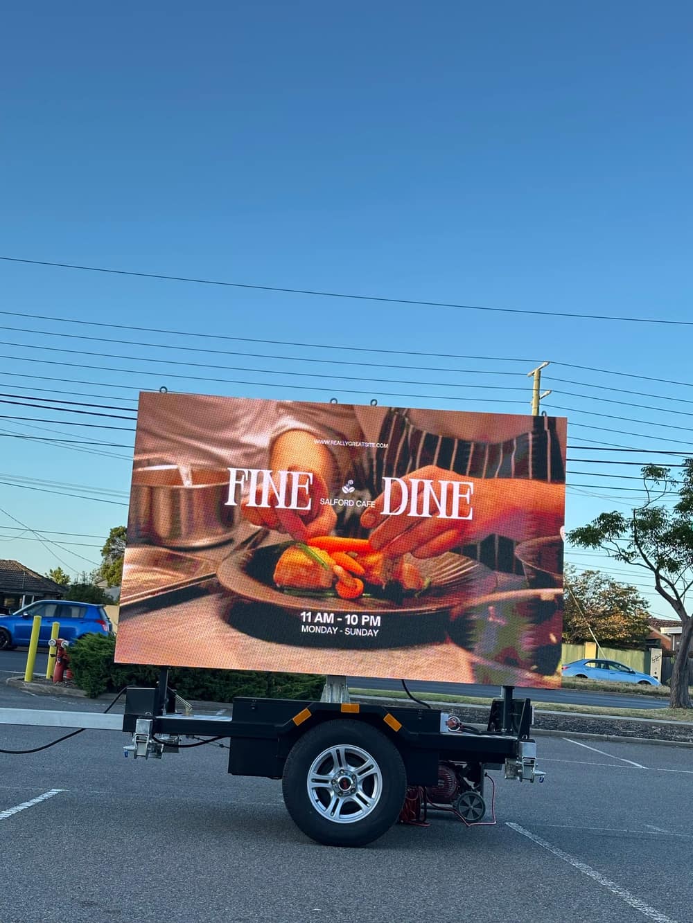 Rear three-quarter view of the LED trailer sign at dusk showing the same full-colour café advertisement