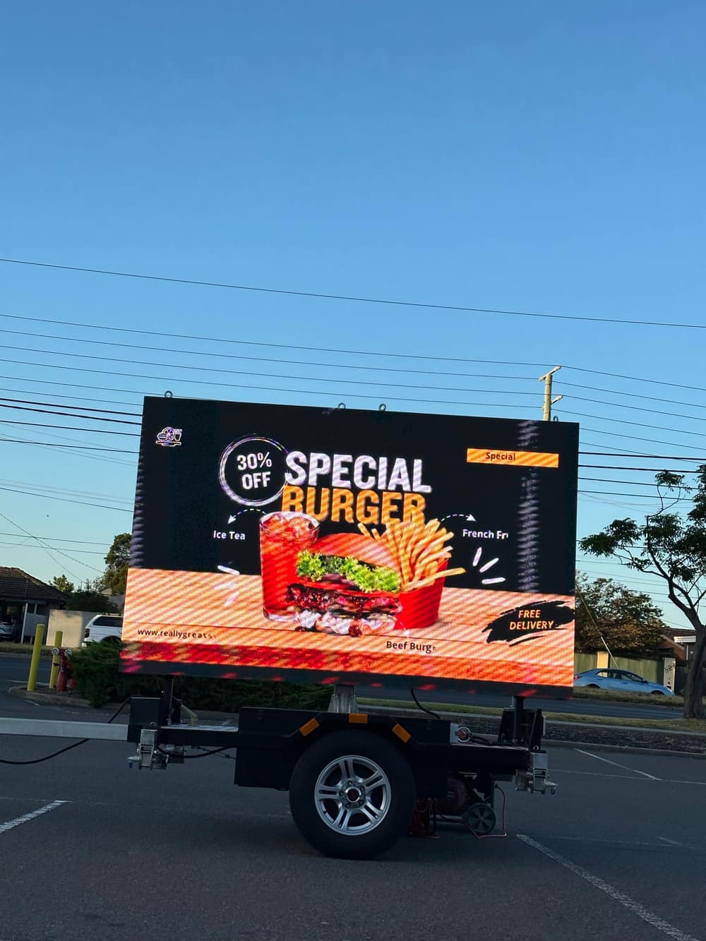 LED trailer sign showing a full-colour fast-food promotion for a burger meal deal with free delivery